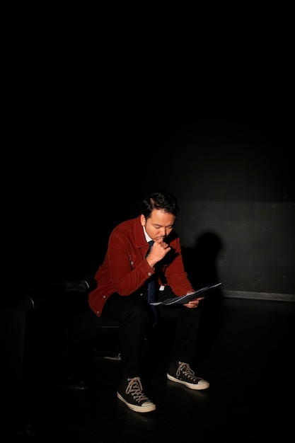 A film critic thoughtfully writing notes in a dark screening room during a movie preview. The light from the screen gently illuminates their face and notepad, suggesting careful analysis and professional assessment.