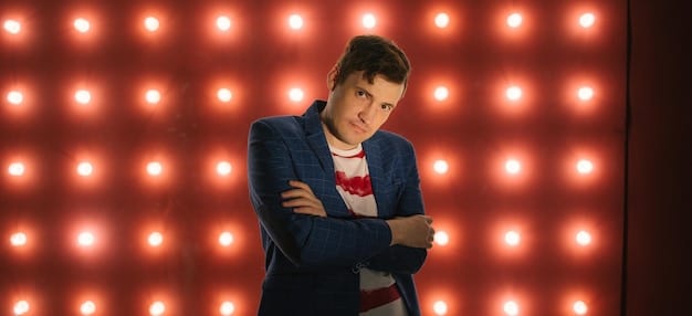 A stand-up comedian on stage looking thoughtful and slightly concerned, with a spotlight shining on them. The backdrop is blurred to focus on the comedian's expression. The image conveys a sense of contemplation about the boundaries of humor.