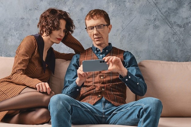 Two people sitting side-by-side on a couch, both holding tablets showing conflicting movie reviews - one showing a very positive review and the other showing a negative one. The background shows a neutral living room setting with soft lighting.